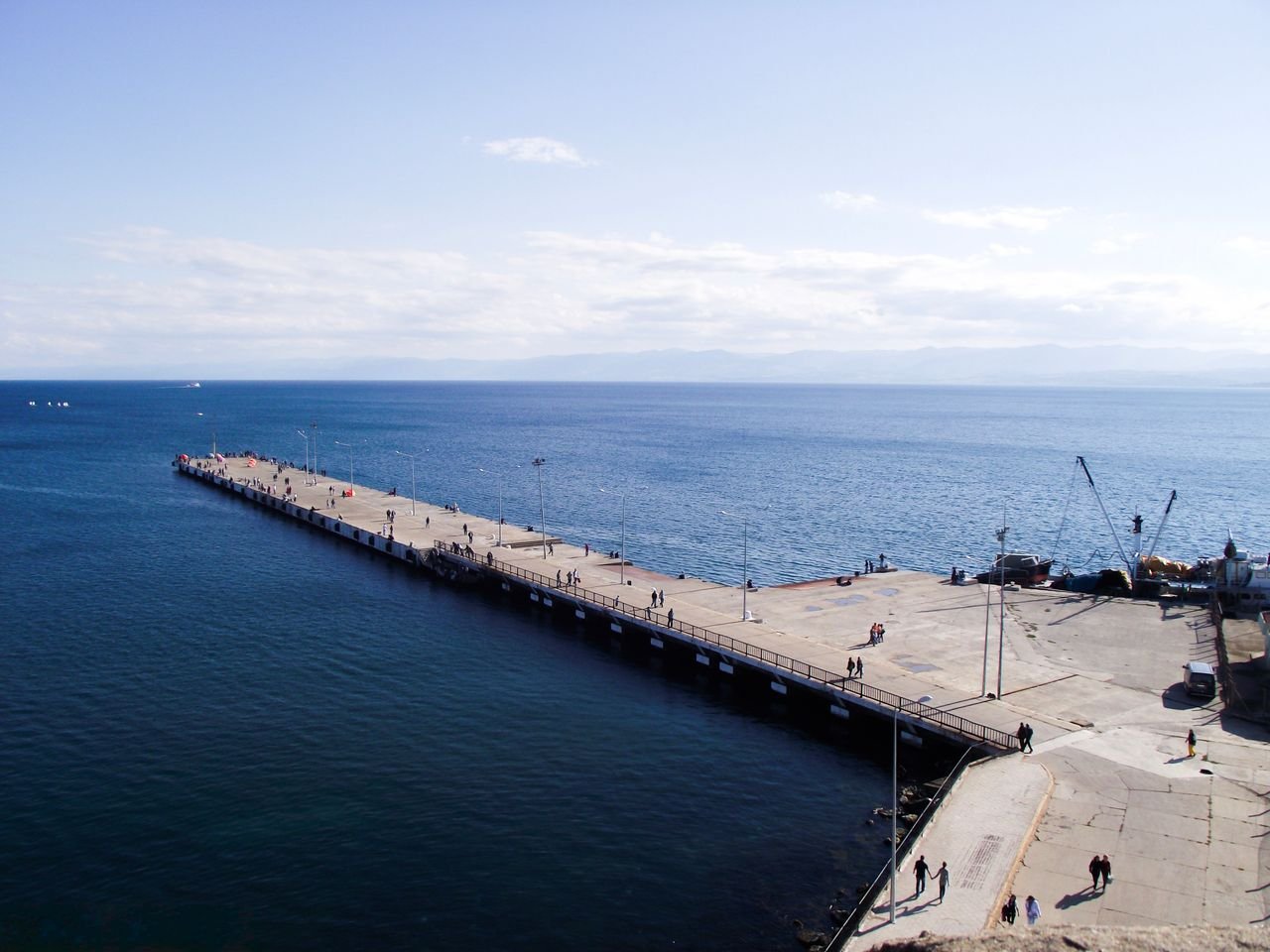 Aerial view of an ocean pier stretching into a calm blue sea under a clear sky.